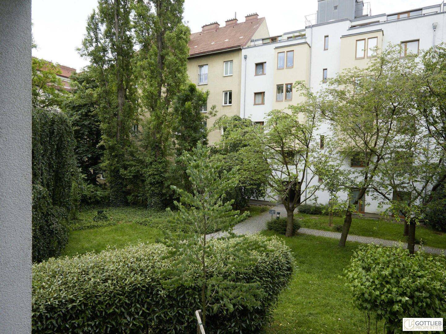 Gepflegter Innenhofgarten mit üppigem Grün, Bäumen und einem gepflasterten Weg zwischen den Gebäuden.