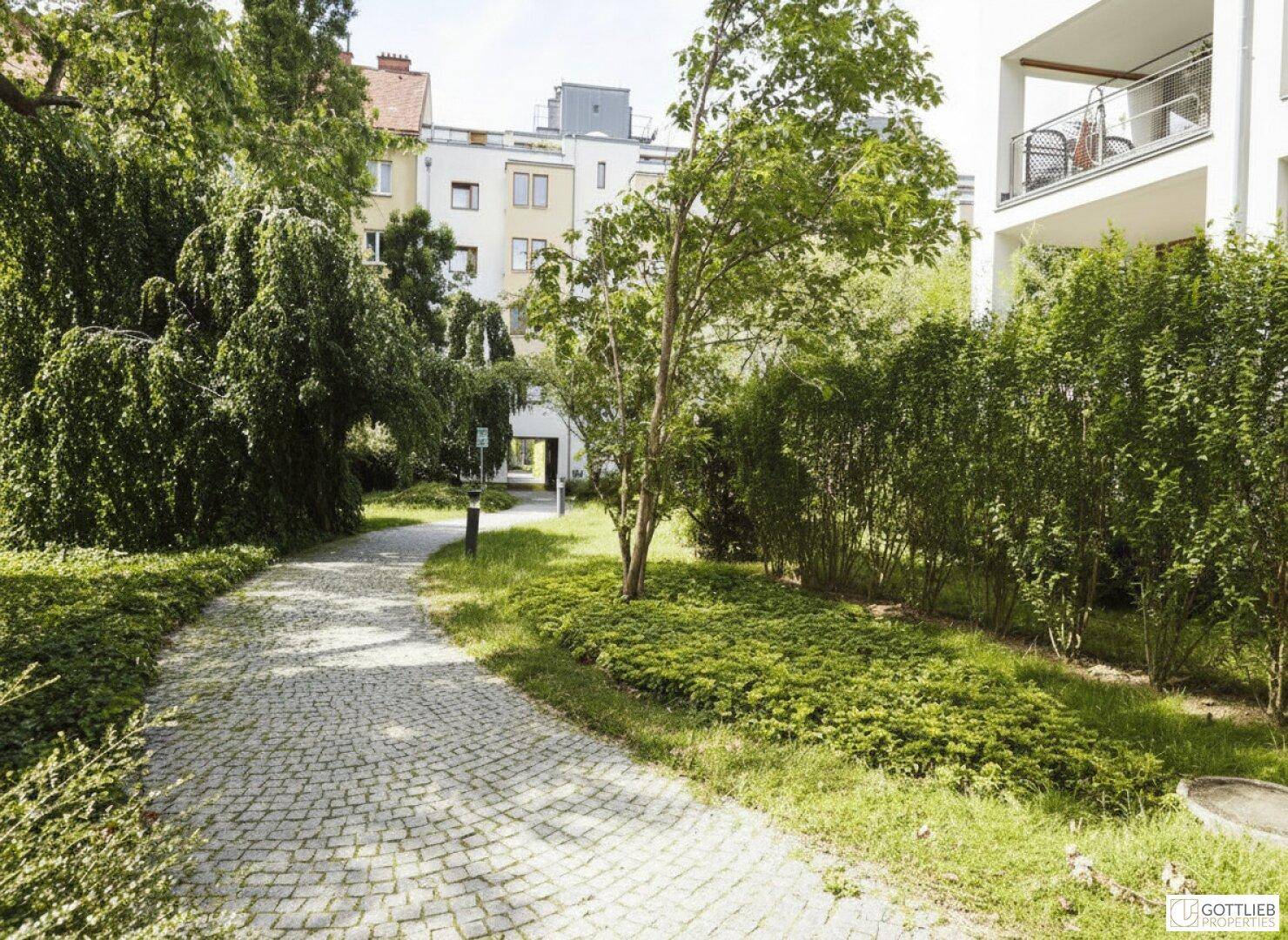 Ruhiger Innenhof mit gepflastertem Weg, umgeben von Bäumen und Sträuchern, bietet Erholung.