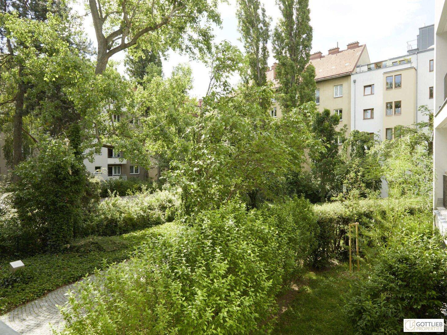 Üppiger grüner Innenhof mit hohen Bäumen und Sträuchern, der eine ruhige Atmosphäre schafft.