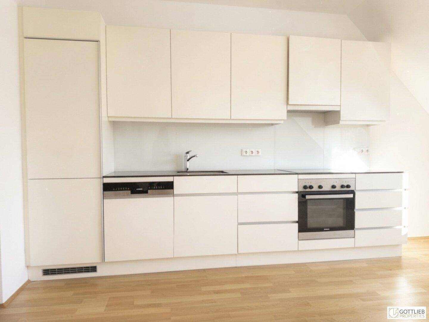 Moderne Einbauküche mit weißen Schränken, integrierten Geräten und dunkler Arbeitsplatte.