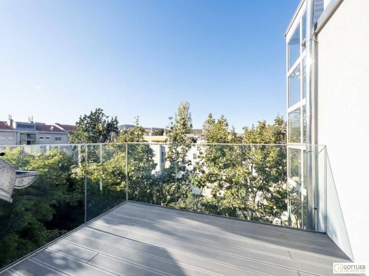 Geräumiger Balkon mit Glasbrüstung und Blick auf die umliegenden Bäume und Gebäude.