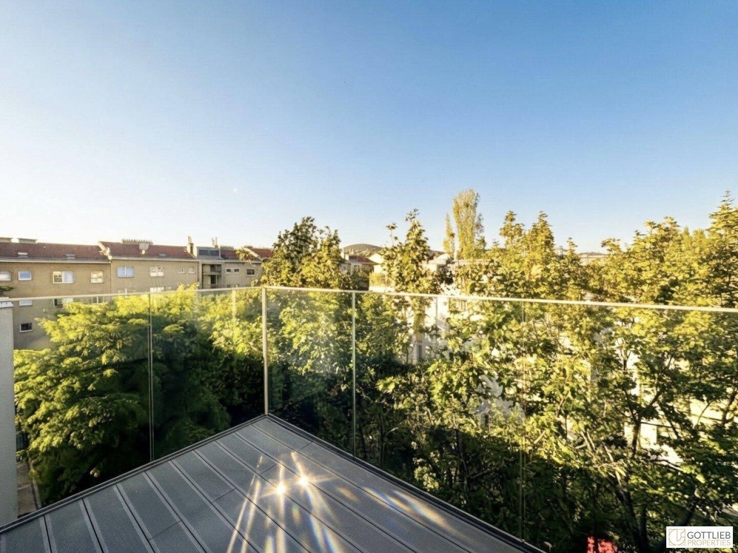Sonniger Balkon mit modernem Glasgeländer und weitem Blick ins Grüne.