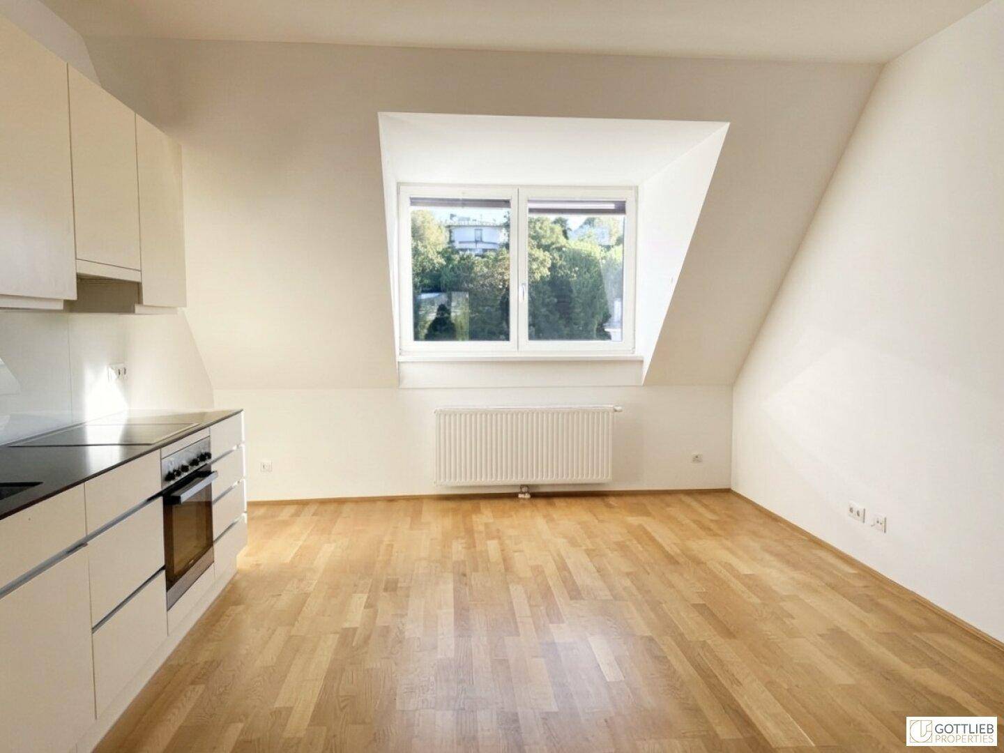 Offener Wohnbereich mit Küchenzeile, Dachschräge und hellem Holzparkett.