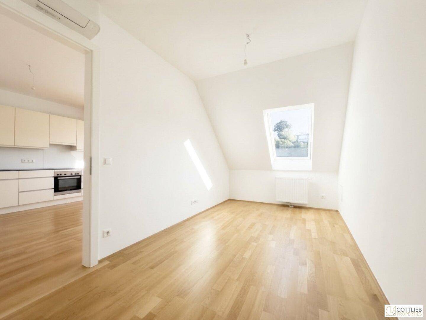 Helles Zimmer mit Dachschräge, Parkettboden und Blick ins Grüne durch das Fenster.