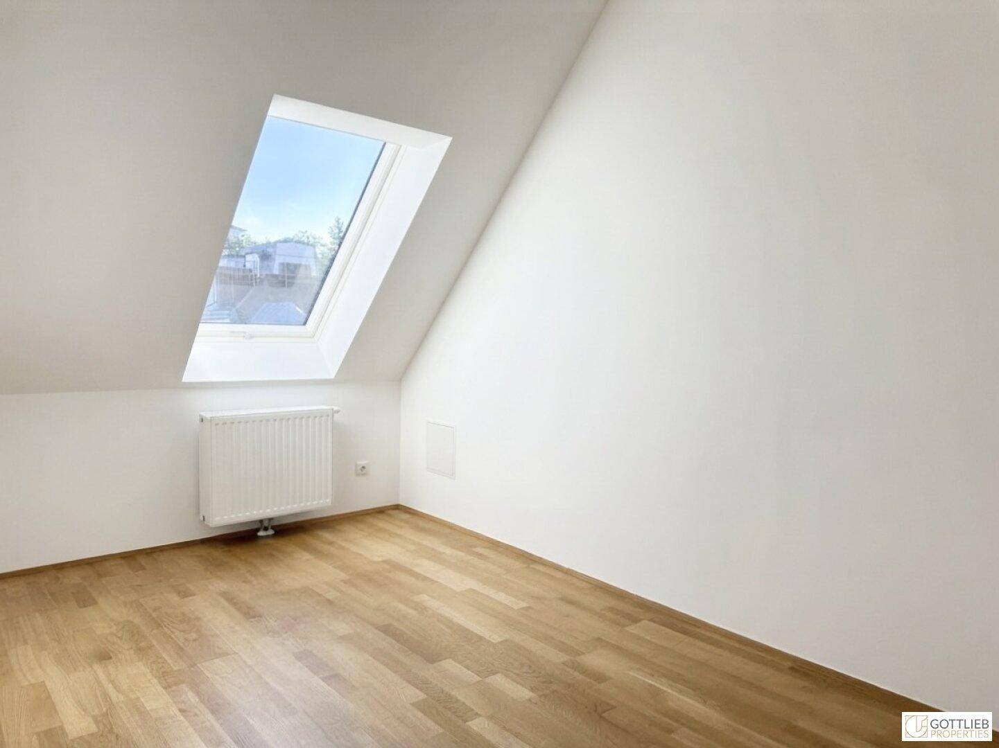 Helles Zimmer mit Dachschräge, Parkettboden und einem Dachfenster für viel Tageslicht.