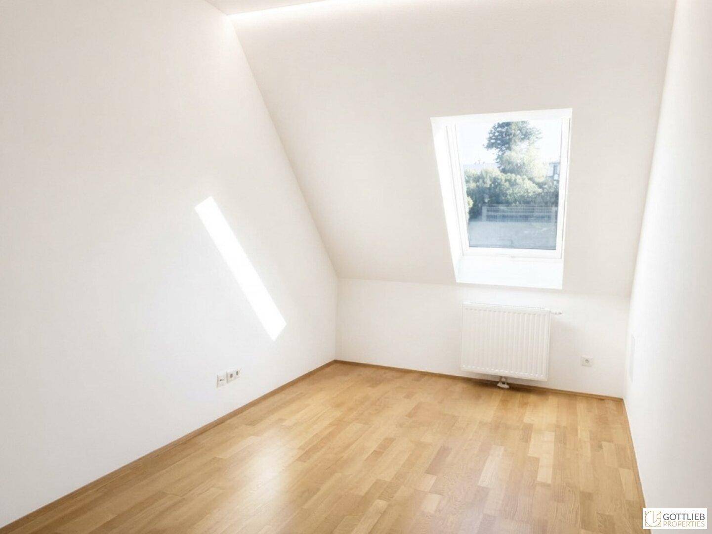 Sonniger Raum mit Dachschräge, Parkettboden und einem Fenster, das viel Licht hereinlässt.