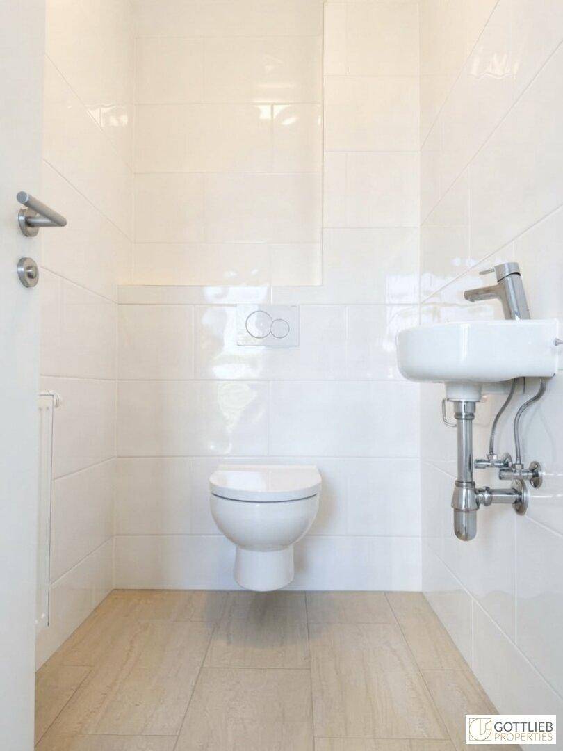 Modernes Gäste-WC mit weißen Fliesen, wandhängendem WC und kleinem Waschbecken.