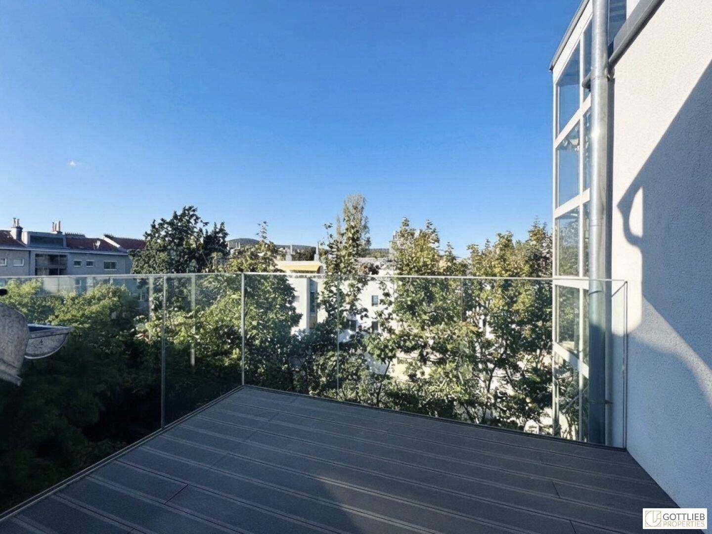 Geräumiger Balkon mit Glasbrüstung und Blick auf die umliegenden Bäume und Gebäude.
