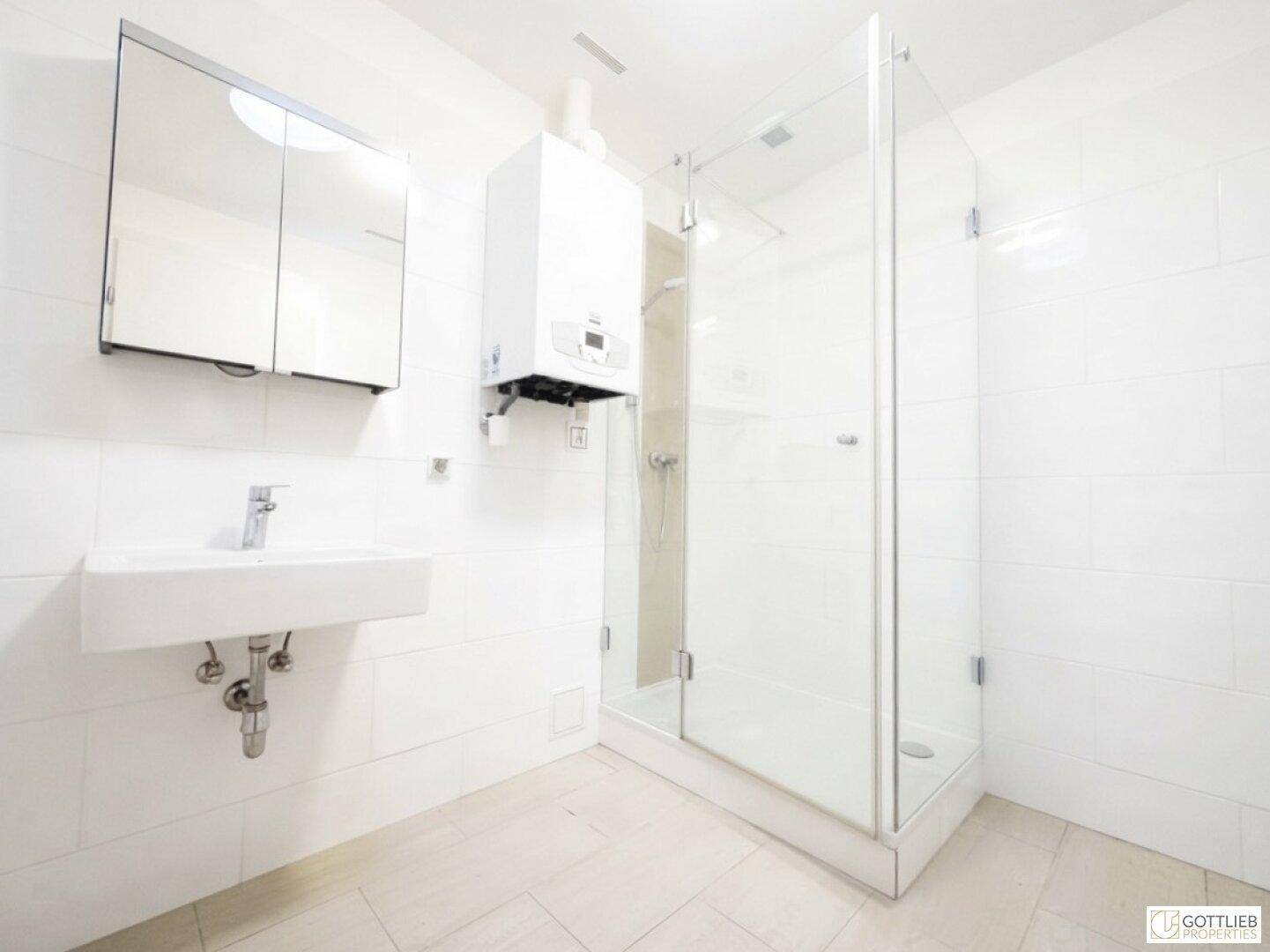 Modernes Badezimmer mit Duschkabine, Waschbecken und Warmwasserbereiter an der Wand.