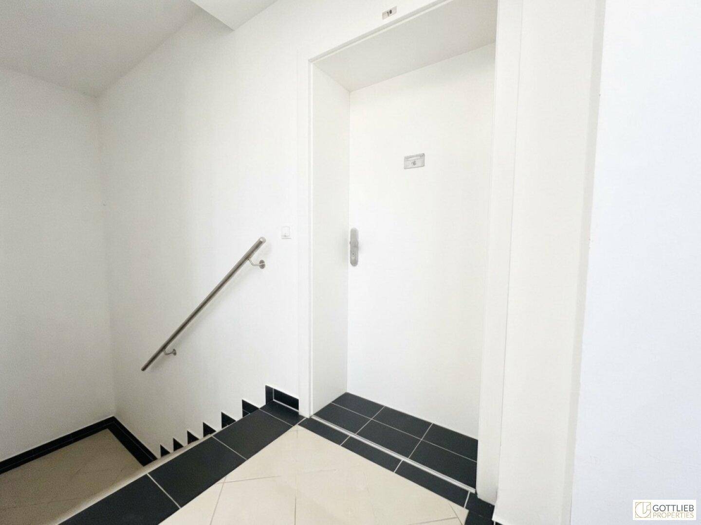 Heller Treppenabsatz mit Aufzugstür und Handlauf, sauber und funktional gestaltet.