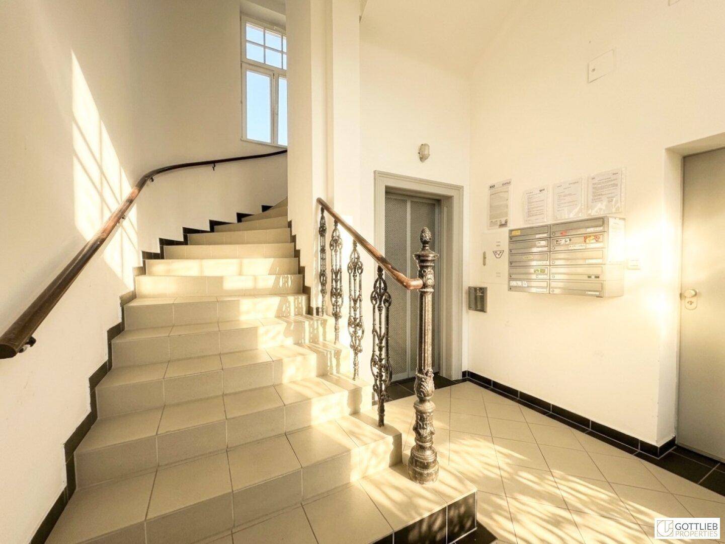 Elegantes Treppenhaus mit geschwungener Treppe, schmiedeeisernem Geländer und Aufzug.