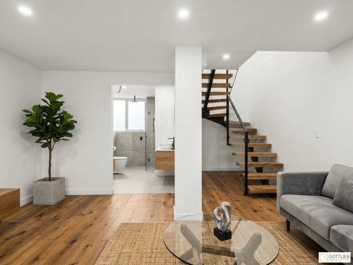 Modernes Wohnzimmer mit Holzboden, offener Treppe und Blick in ein stilvolles Badezimmer.