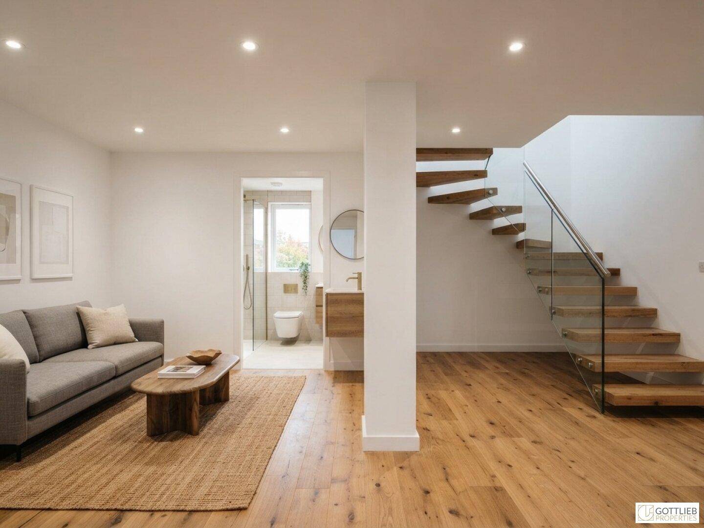 Helles Wohnzimmer mit Holzboden, moderner Treppe und angrenzendem Badezimmer mit Fenster.