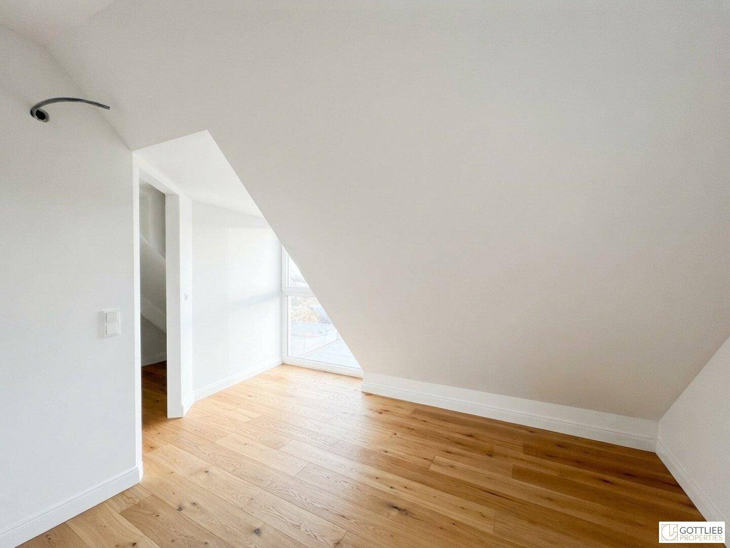 Leerer Raum im Dachgeschoss mit Holzboden, weißen Wänden und Schrägdach.