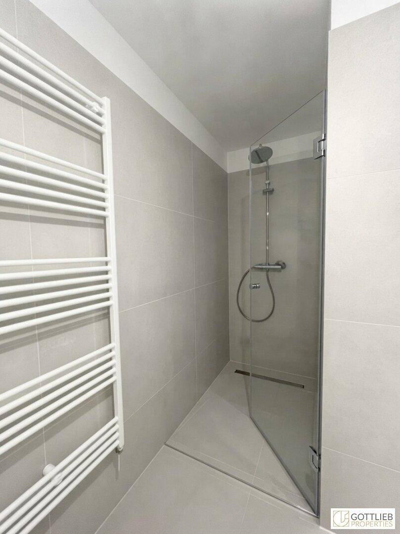 Modernes Badezimmer mit begehbarer Dusche, grauen Fliesen und beheiztem Handtuchhalter.