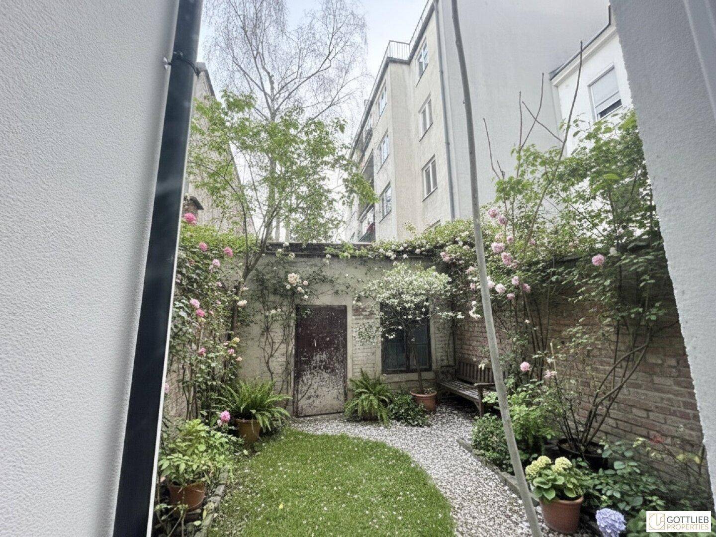 Kleiner, begrünter Innenhof mit Kiesweg, Sitzbank und bewachsenen Wänden.