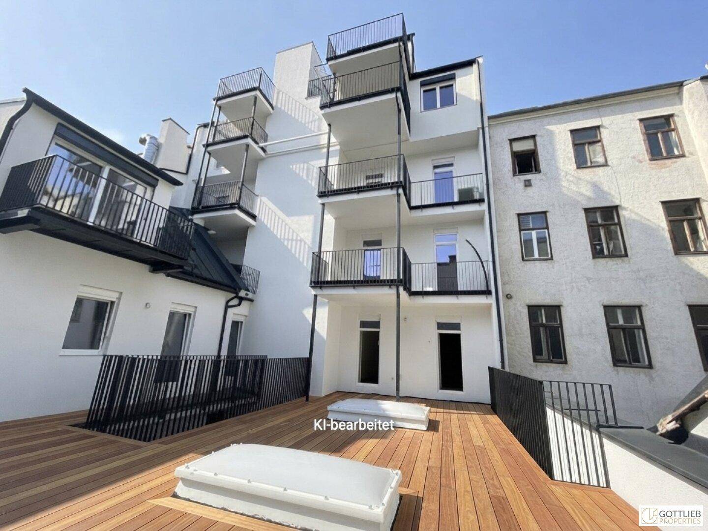 Große Holzterrasse im Innenhof mit Blick auf die modernen Balkone eines sanierten Gebäudes.