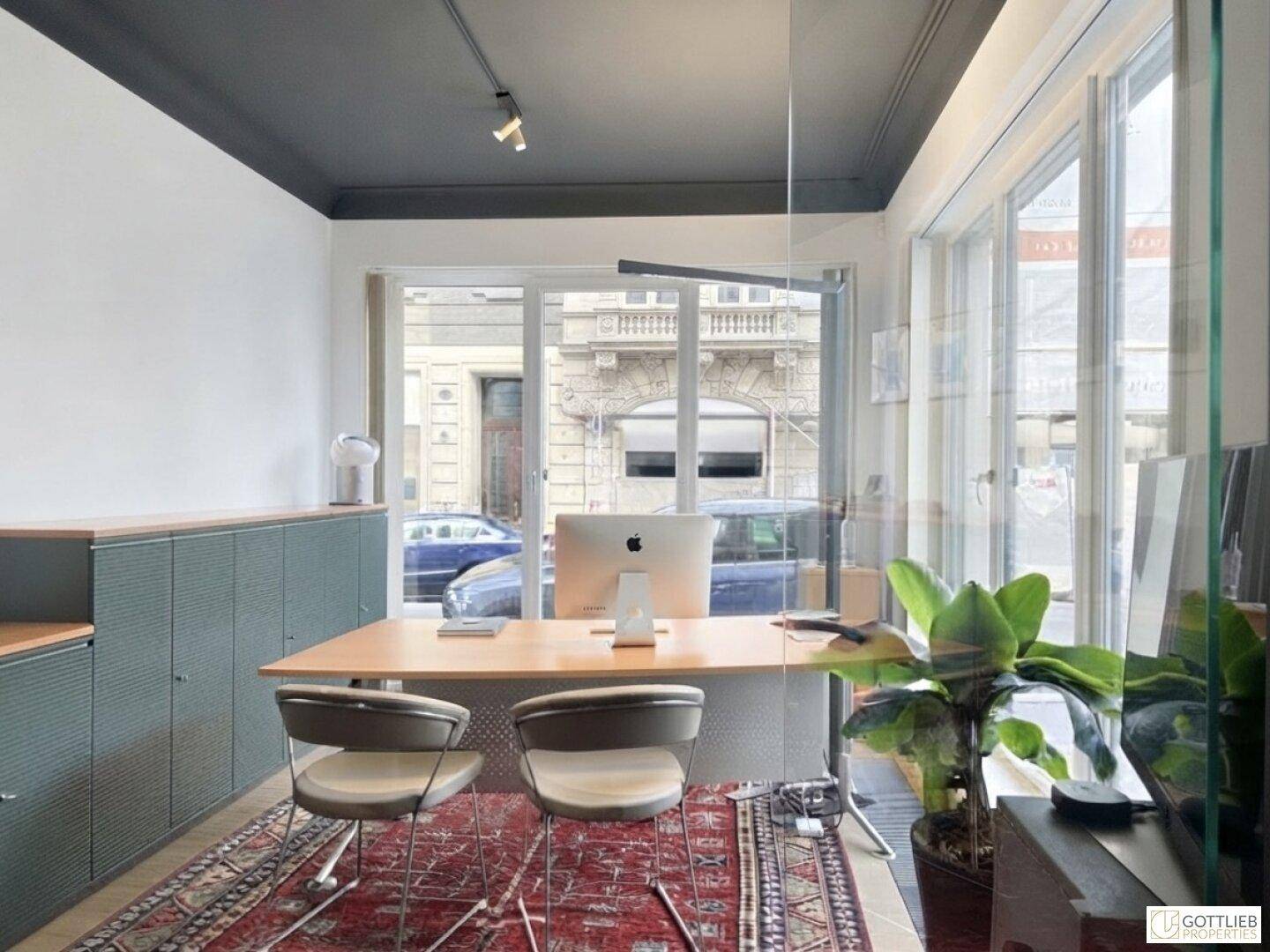 Individuelles Büro mit Schreibtisch, zwei Stühlen und großem Fenster mit Blick auf die Straße.
