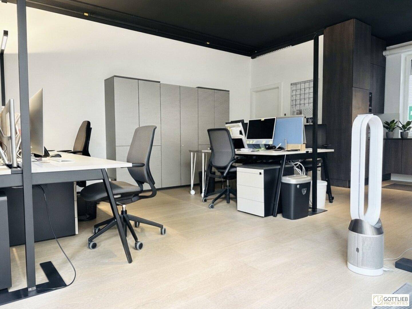 Geräumiges Büro mit mehreren Arbeitsplätzen, Stauraum und dunkler Decke, helles Holzparkett.
