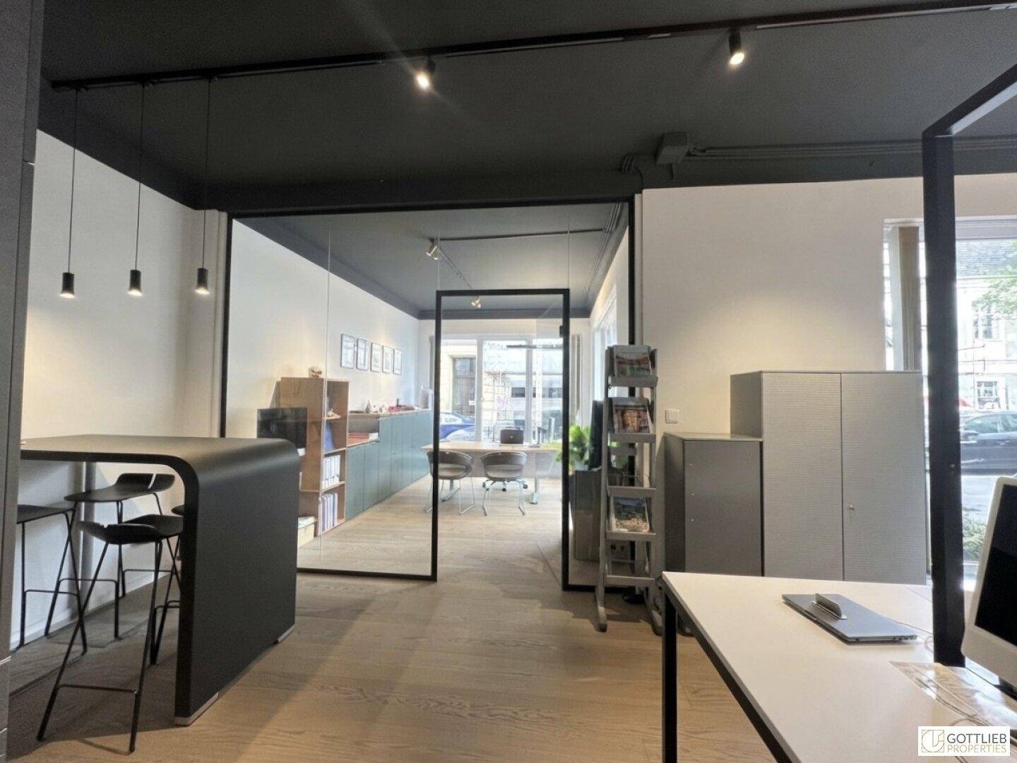 Großraumbüro mit Glasabtrennungen, Stehtischen und Blick in einen weiteren Bürobereich.
