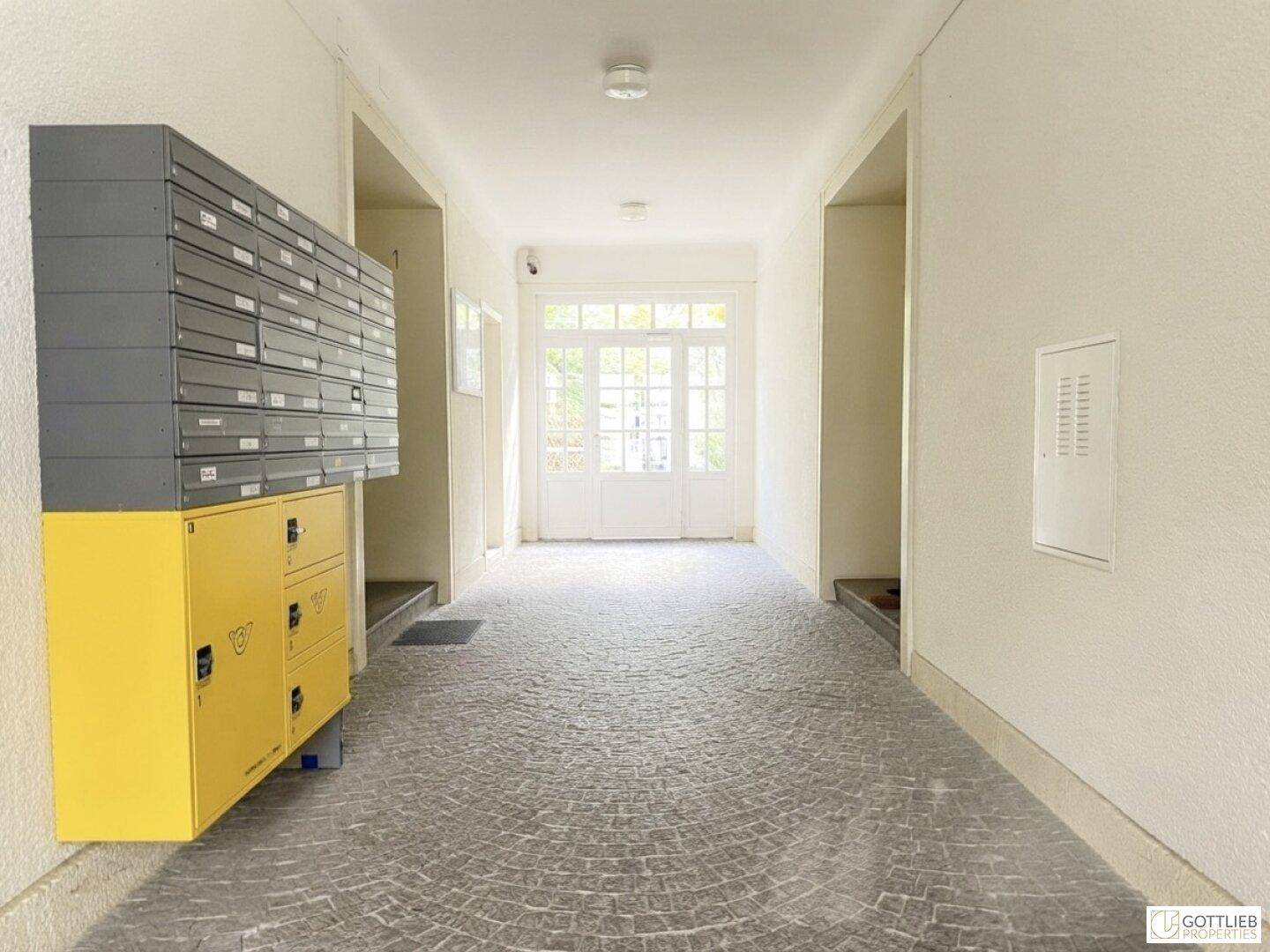 Heller Eingangsbereich eines Gebäudes mit Briefkästen und Blick durch Glastüren ins Freie.