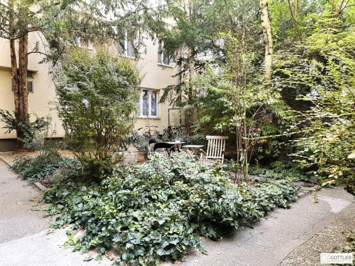 Grüner Innenhofgarten mit Bäumen, Sträuchern und einer kleinen Sitzgelegenheit im Freien.