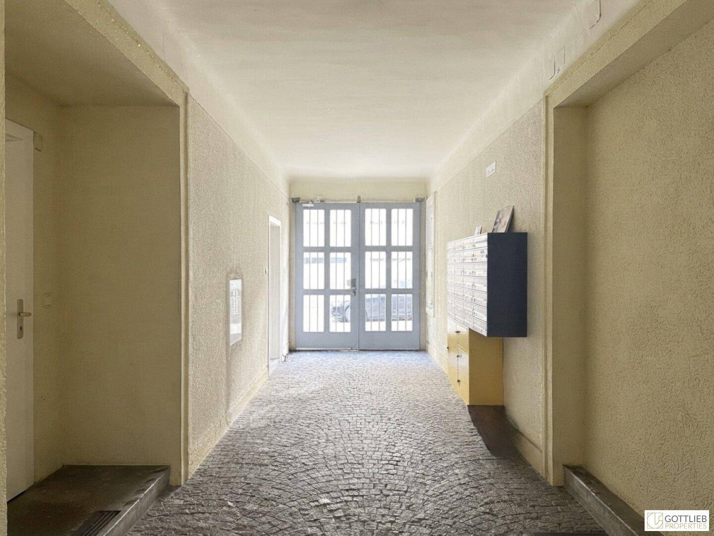 Heller Eingangsbereich eines Gebäudes mit Briefkästen und Blick durch Glastüren ins Freie.