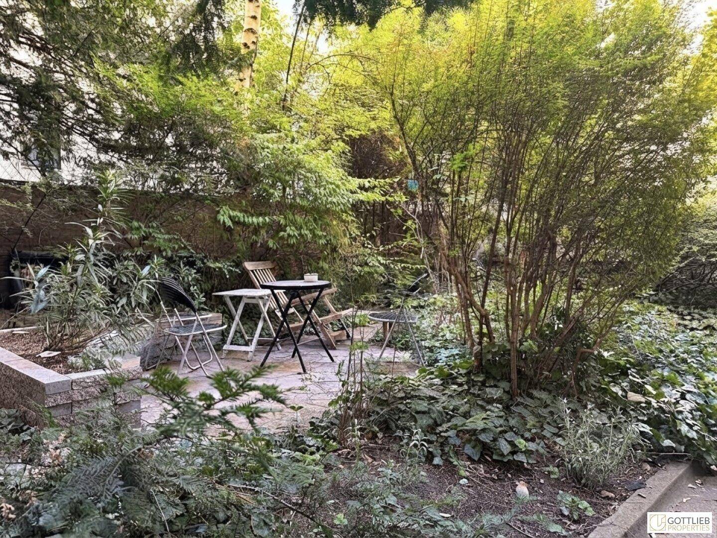 Grüner Innenhofgarten mit Bäumen, Sträuchern und einer kleinen Sitzgelegenheit im Freien.