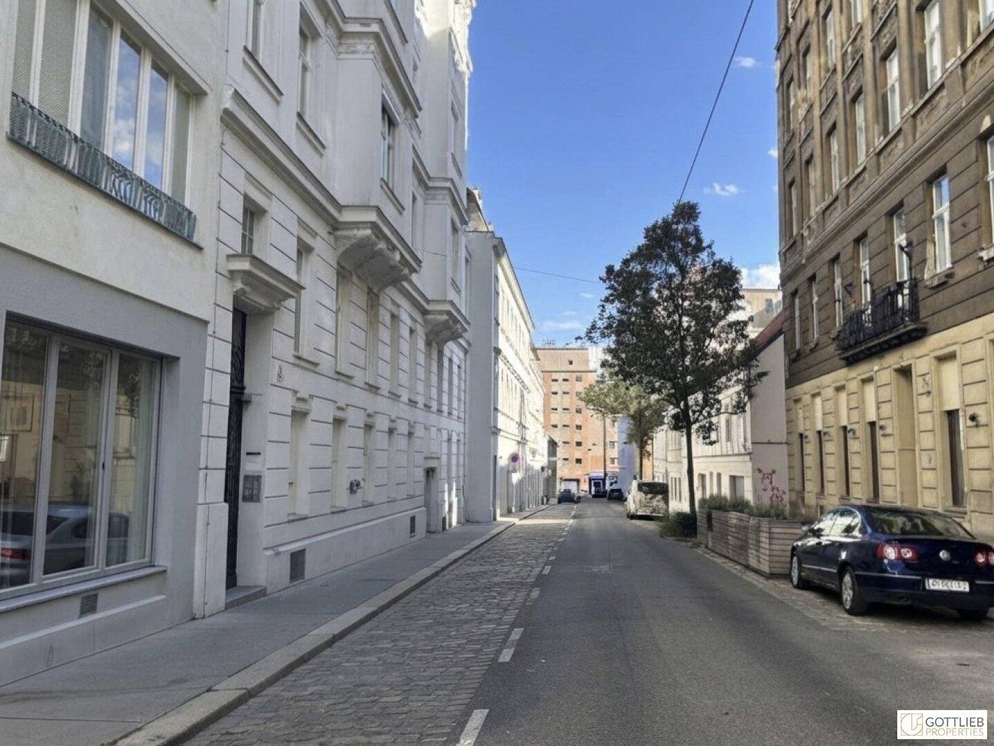 Historische Straße mit Gebäuden, einem geparkten Auto und klarem blauem Himmel.