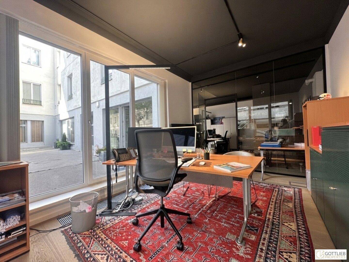 Modernes Büro mit Schreibtisch, Bürostuhl und großem Fenster mit Blick auf einen Innenhof.