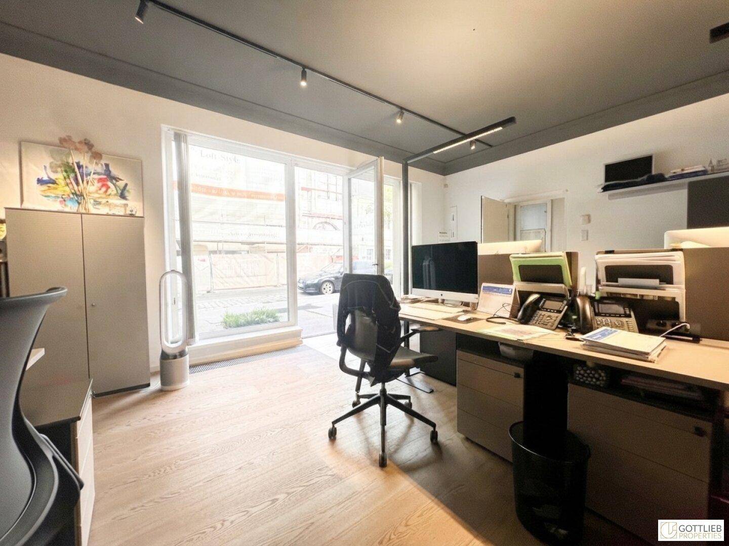 Helles Büro mit Arbeitsplatz, Computer und großer Glastür, die nach draußen führt.