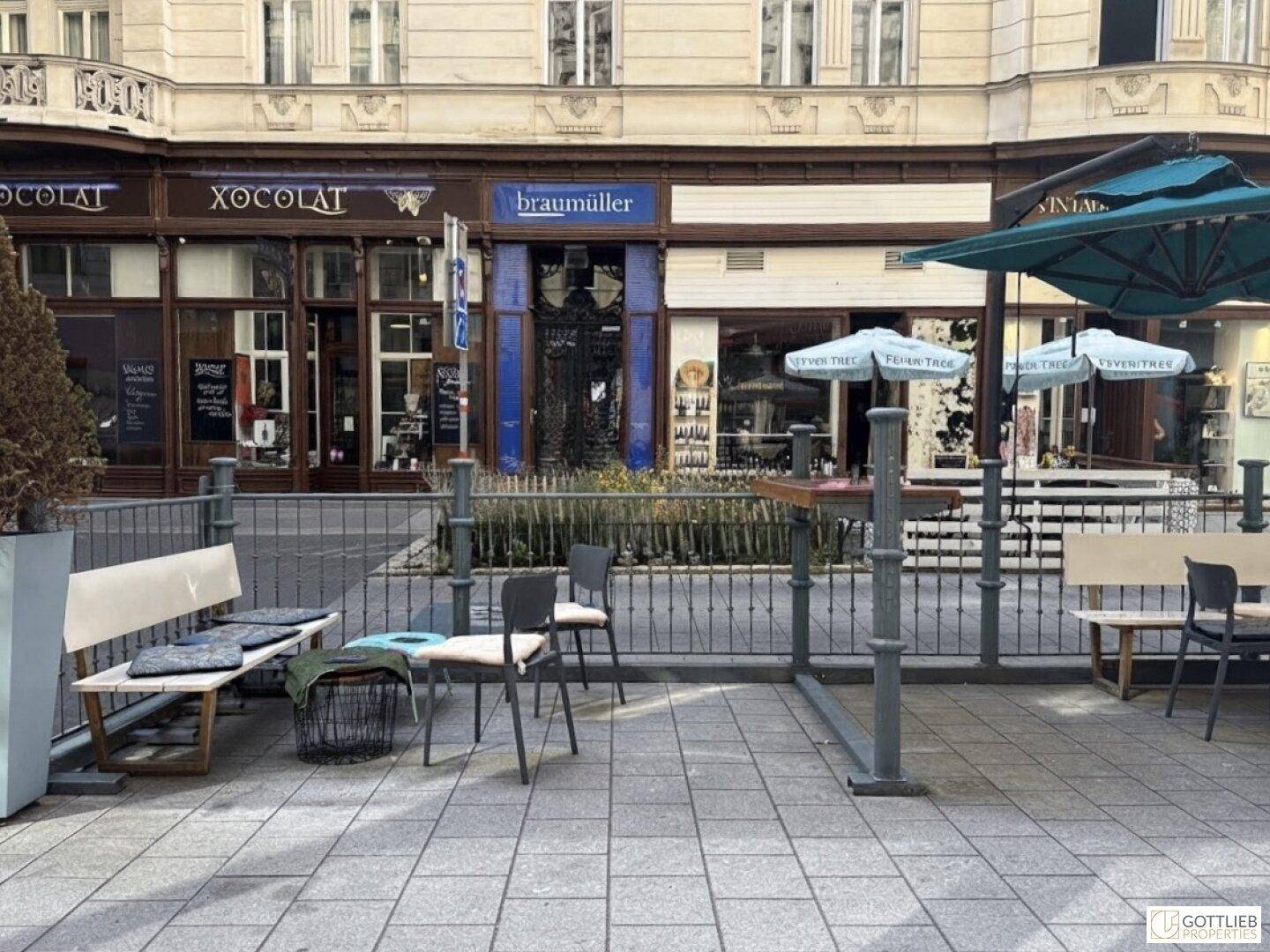 Gemütlicher Außenbereich mit Tischen, Stühlen und Sonnenschirmen vor einer Ladenfassade.