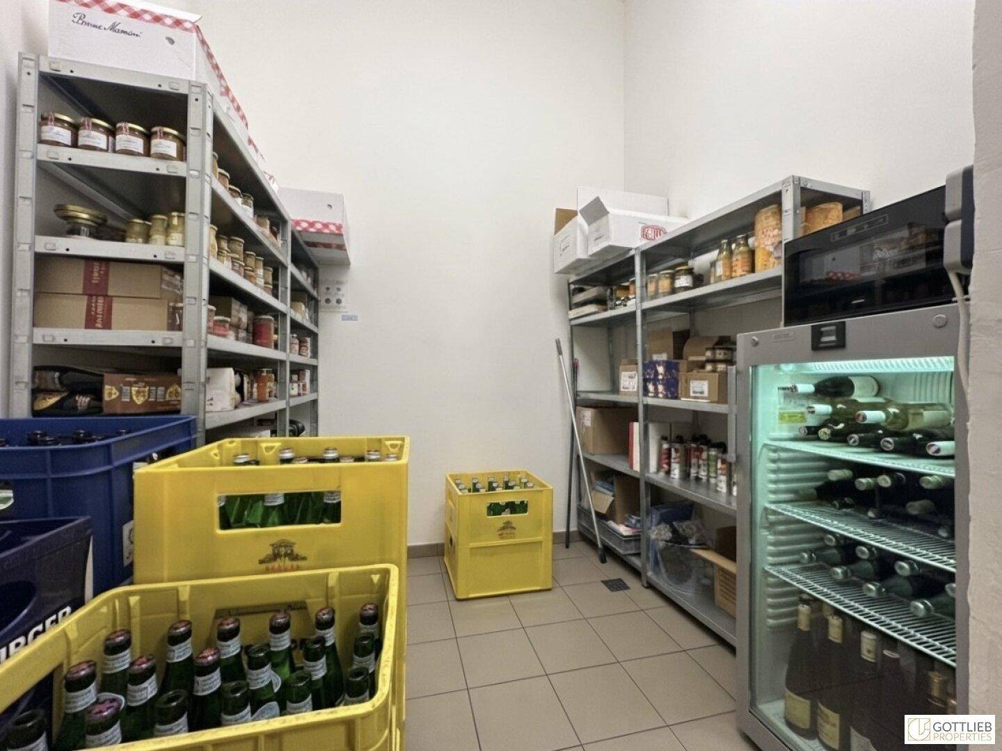 Lagerraum mit Metallregalen, Kisten und einem gewerblichen Kühlschrank für Getränke und Vorräte.