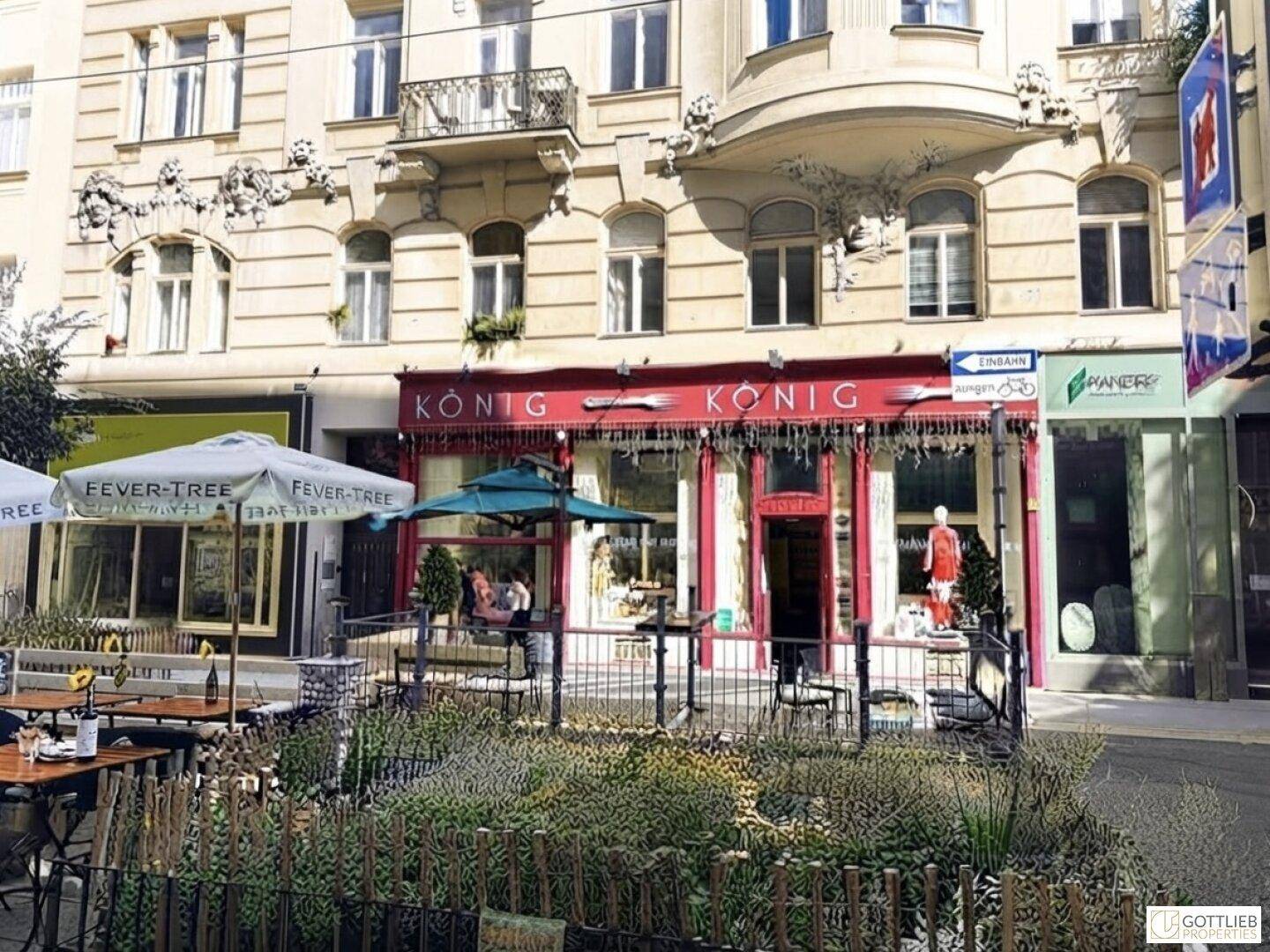 Eine belebte Straße mit Geschäften, Außengastronomie und historischen Gebäuden unter blauem Himmel.
