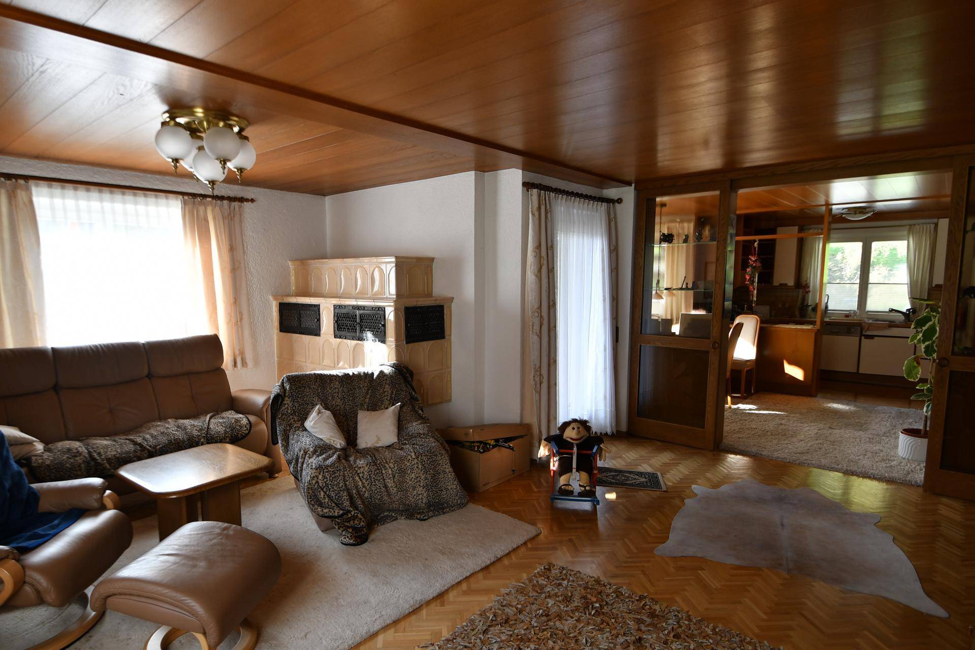 Gemütliches Wohnzimmer mit Holzboden, Holzdecke und traditionellem Kachelofen.