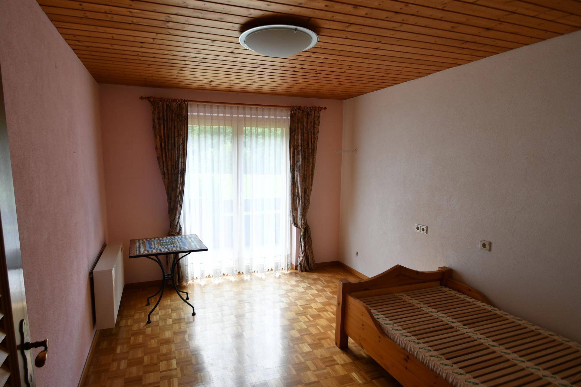 Helles Schlafzimmer mit Holzboden, Holzdecke und großem Fenster.