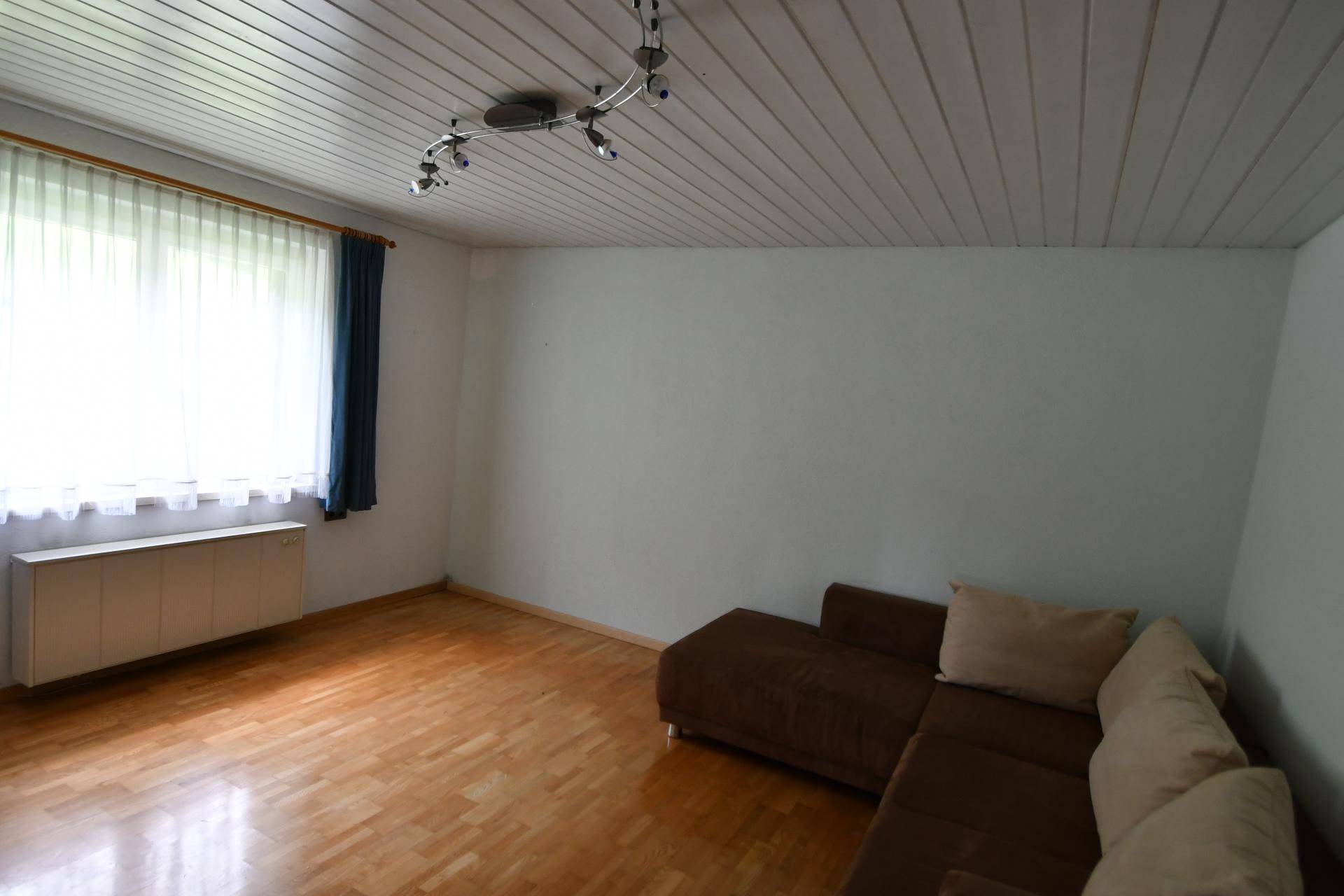 Heller Raum mit Holzboden, weißer Decke und großem Fenster.