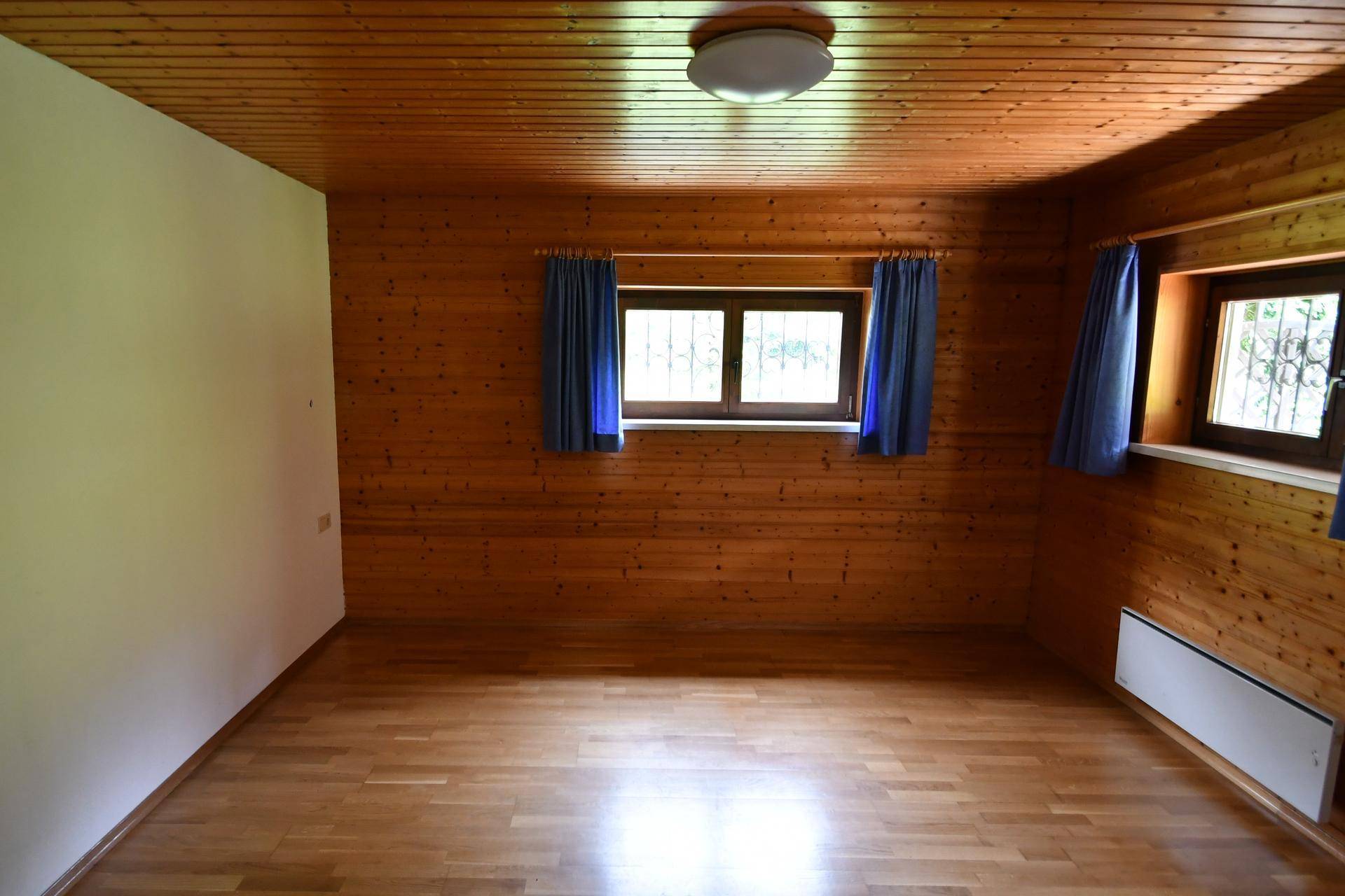 Geräumiges Schlafzimmer mit Holzwänden, Holzdecke und zwei Fenstern.