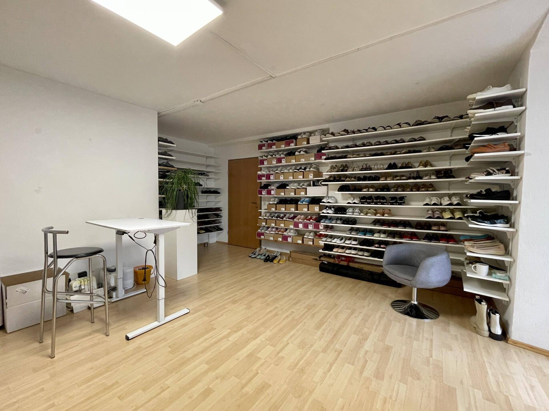 Geräumiger Mehrzweckraum mit umfangreichen Schuhregalen, hellem Holzboden und einem Stehtisch mit Hockern.