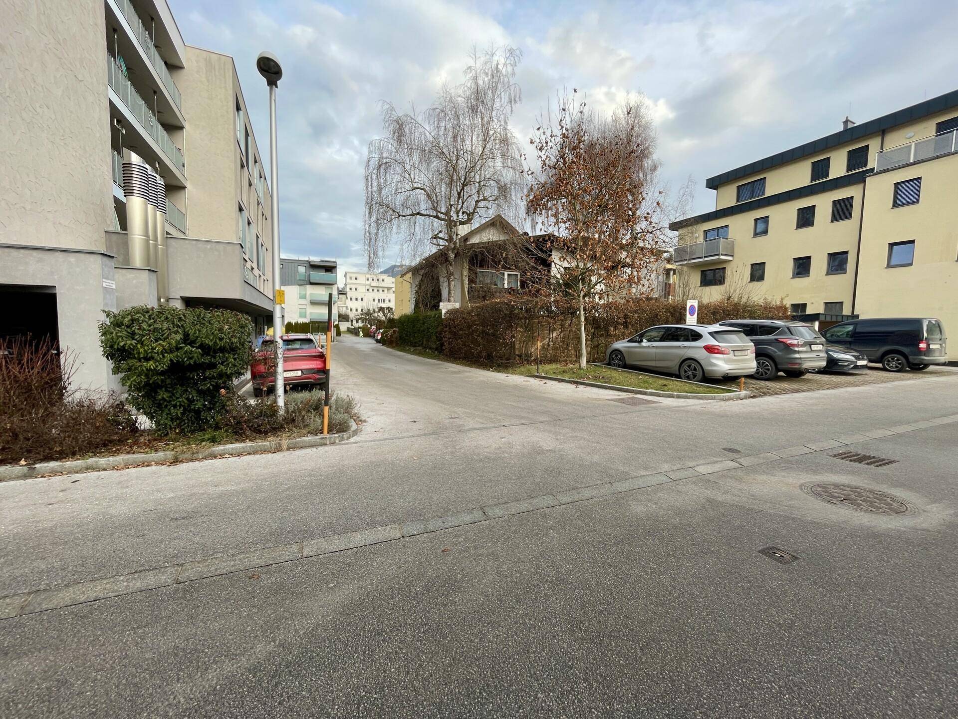 Wohnstraße mit geparkten Autos und modernen Mehrfamilienhäusern unter bewölktem Himmel.