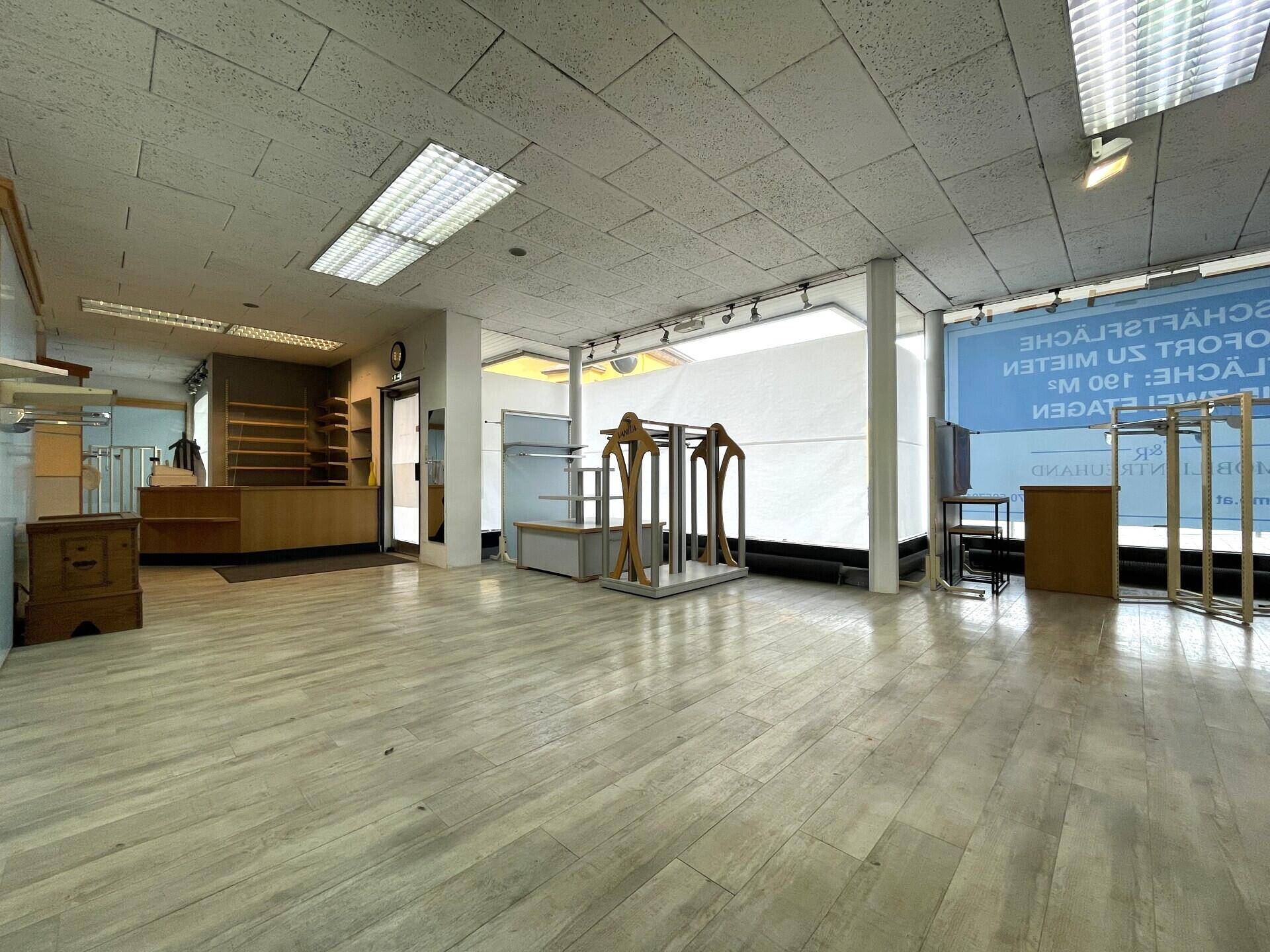 Weiterer Blick in den Ladenbereich mit Schaufenstern, abgehängter Decke und verschiedenen Präsentationsständern.