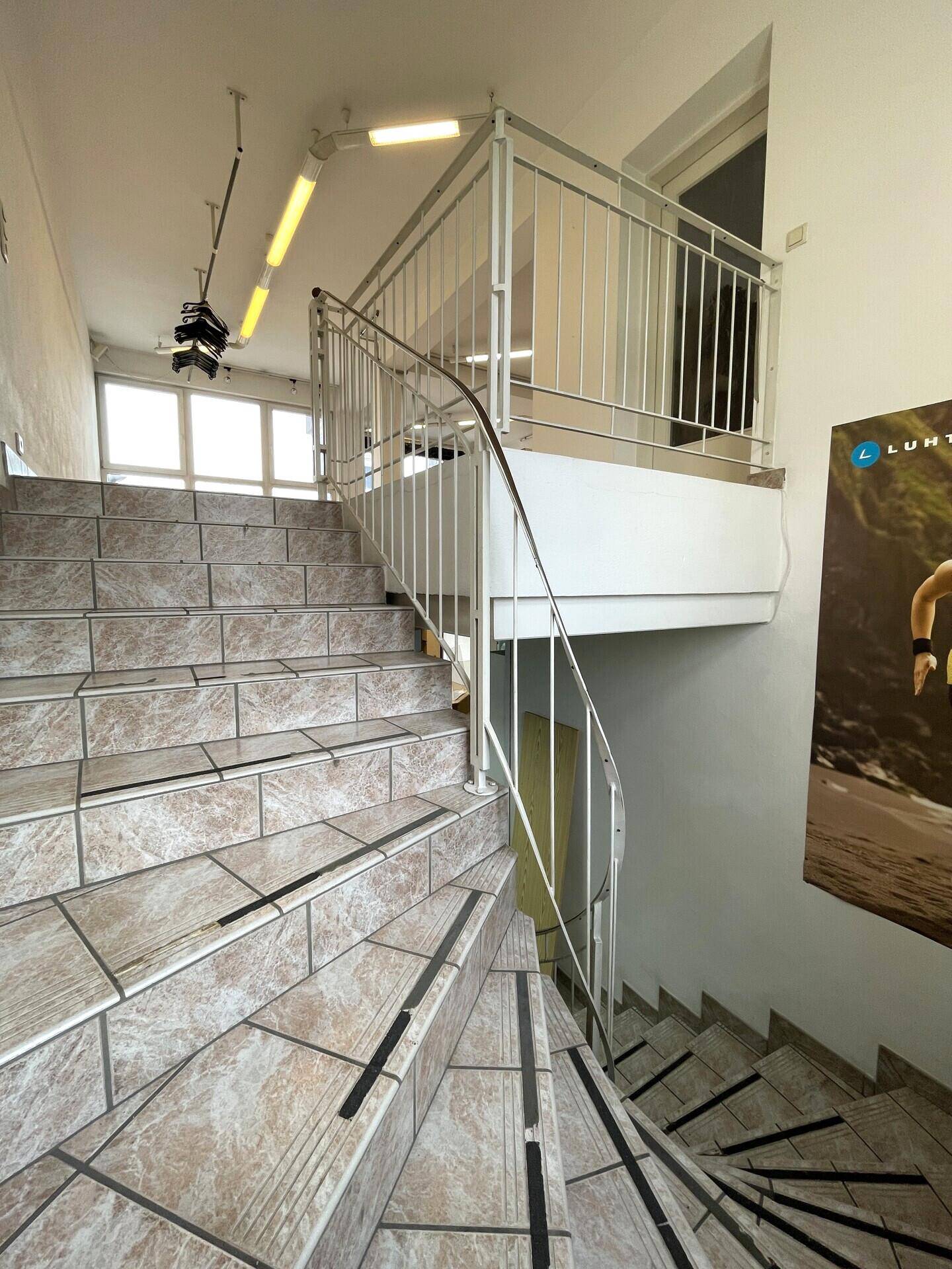 Treppenaufgang mit gefliesten Stufen, Metallgeländer und einem großen Werbebanner an der Wand.