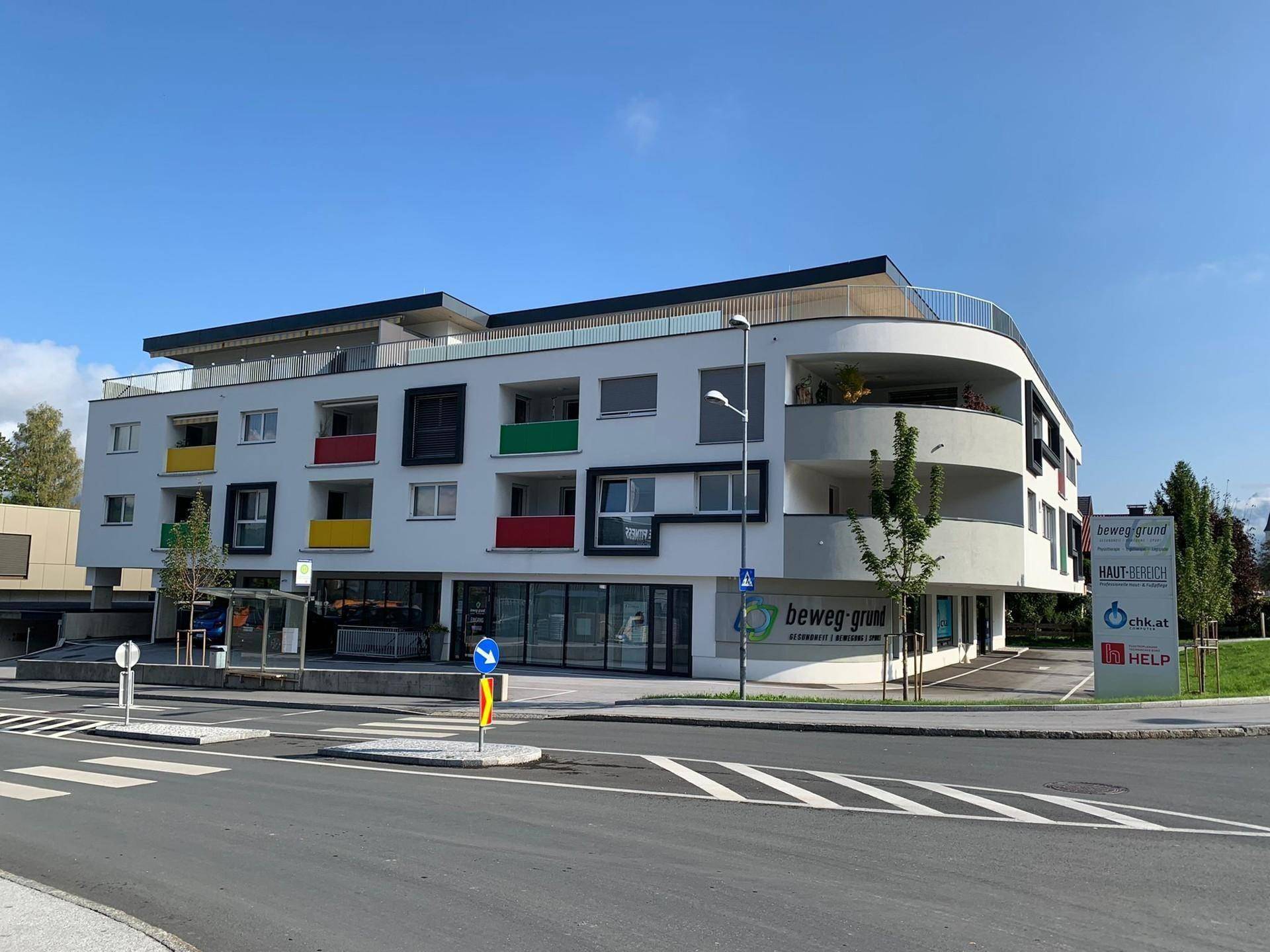 Modernes Wohn- und Geschäftsgebäude mit farbigen Balkonen, klaren Linien und Flachdacharchitektur.