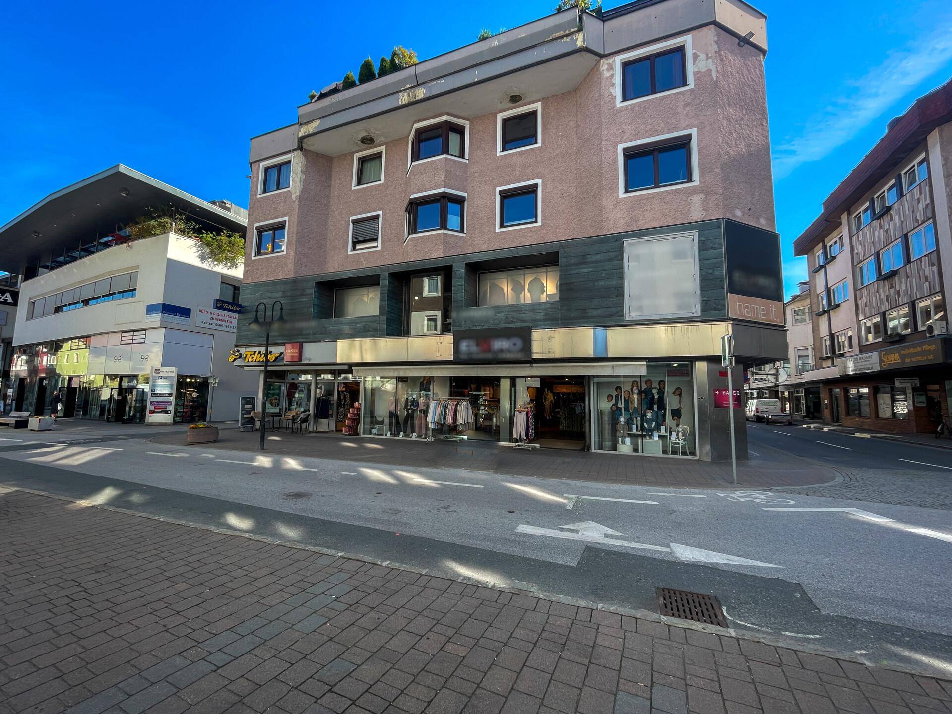 Gebäude mit Ladenfronten im Erdgeschoss und Wohnungen darüber, an einer belebten Straße gelegen.