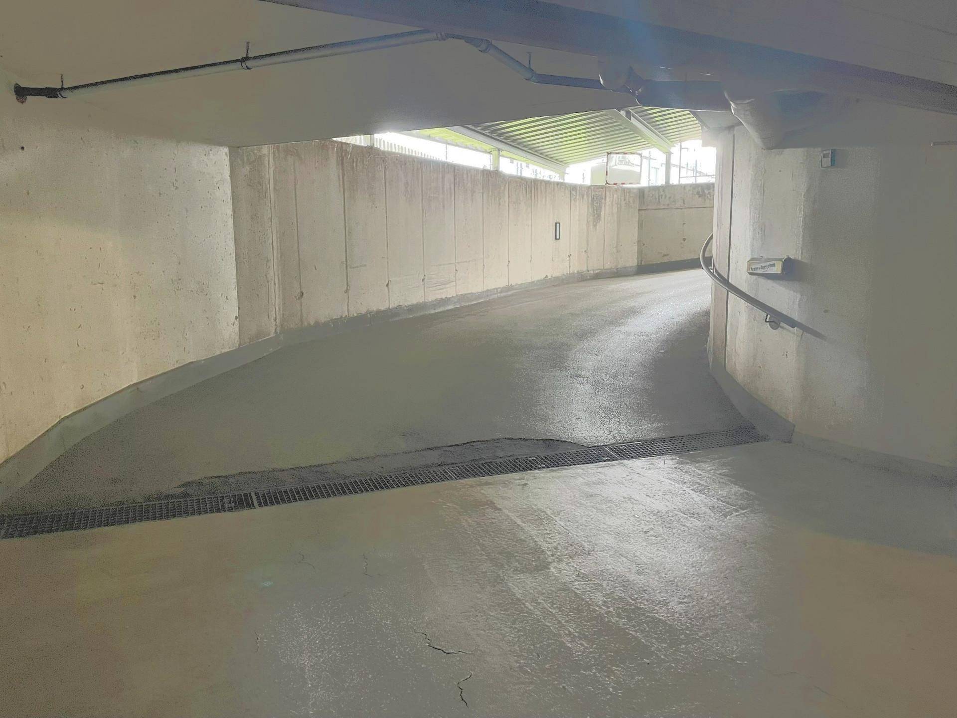 Betonierte Rampe führt aus der Tiefgarage ins Freie, mit Handlauf an der Seite.