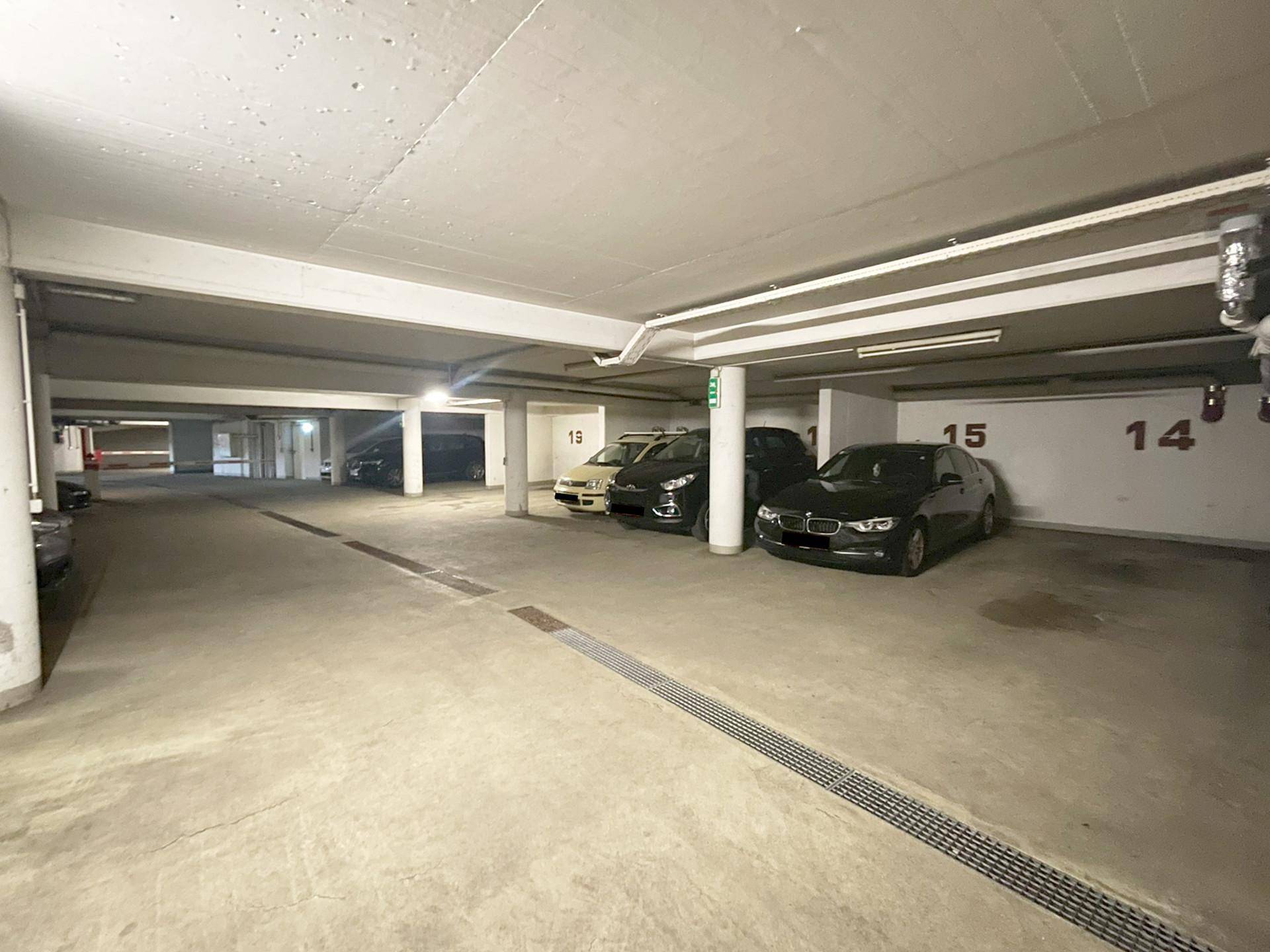 Geräumige Tiefgarage mit mehreren geparkten Fahrzeugen und Entwässerungsrinnen im Boden.