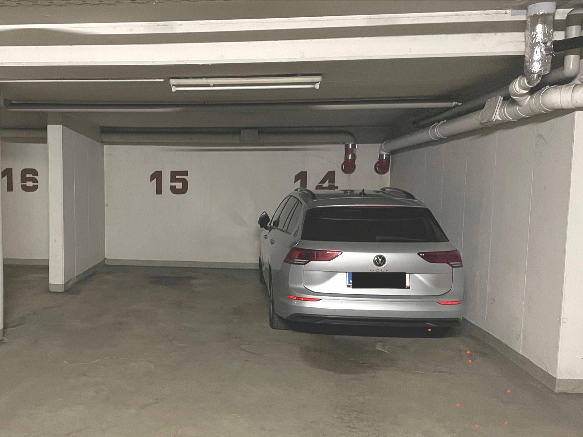Tiefgaragenstellplatz mit einem geparkten Auto und sichtbaren Leitungen an der Decke.