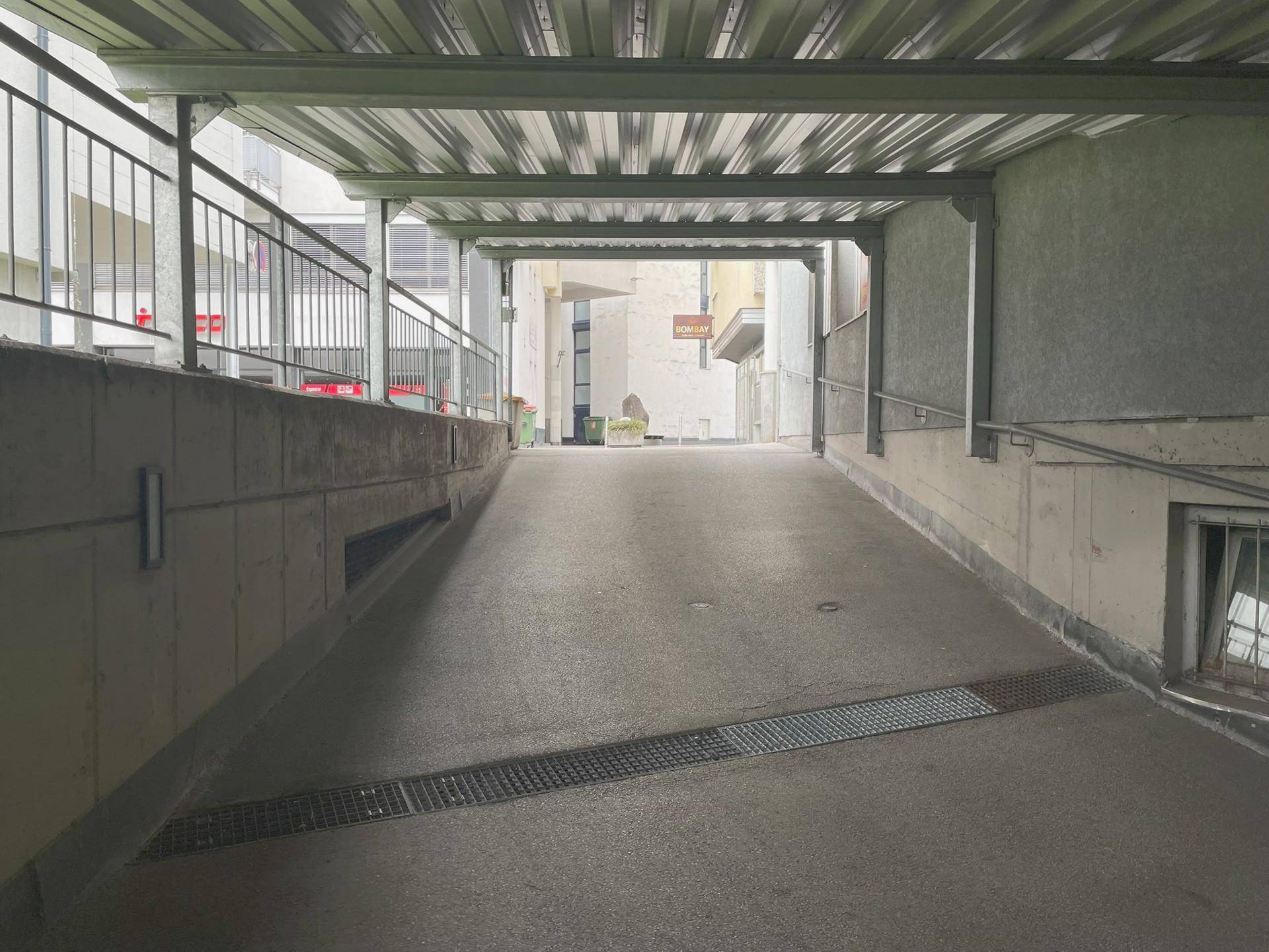 Überdachte Zufahrtsrampe zur Tiefgarage mit Metallkonstruktion und Entwässerungsrinne.