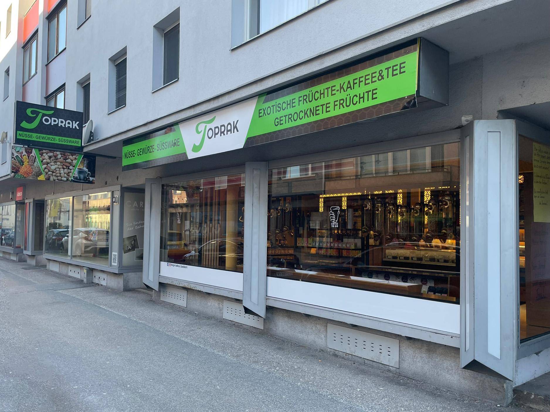 Nahaufnahme der Geschäftsfassade mit großen Schaufenstern und Beschilderung des Ladens Toprak.