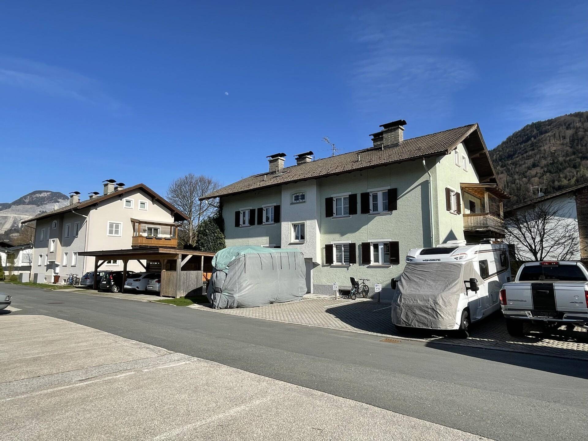 Wohngebäude mit Carports und geparkten Fahrzeugen in einer bergigen Landschaft unter blauem Himmel.